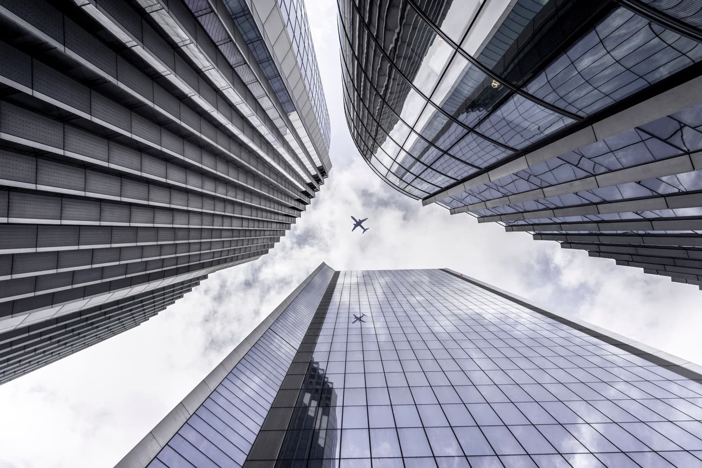 Three sky scrapers shown from below with plane flying overhead 