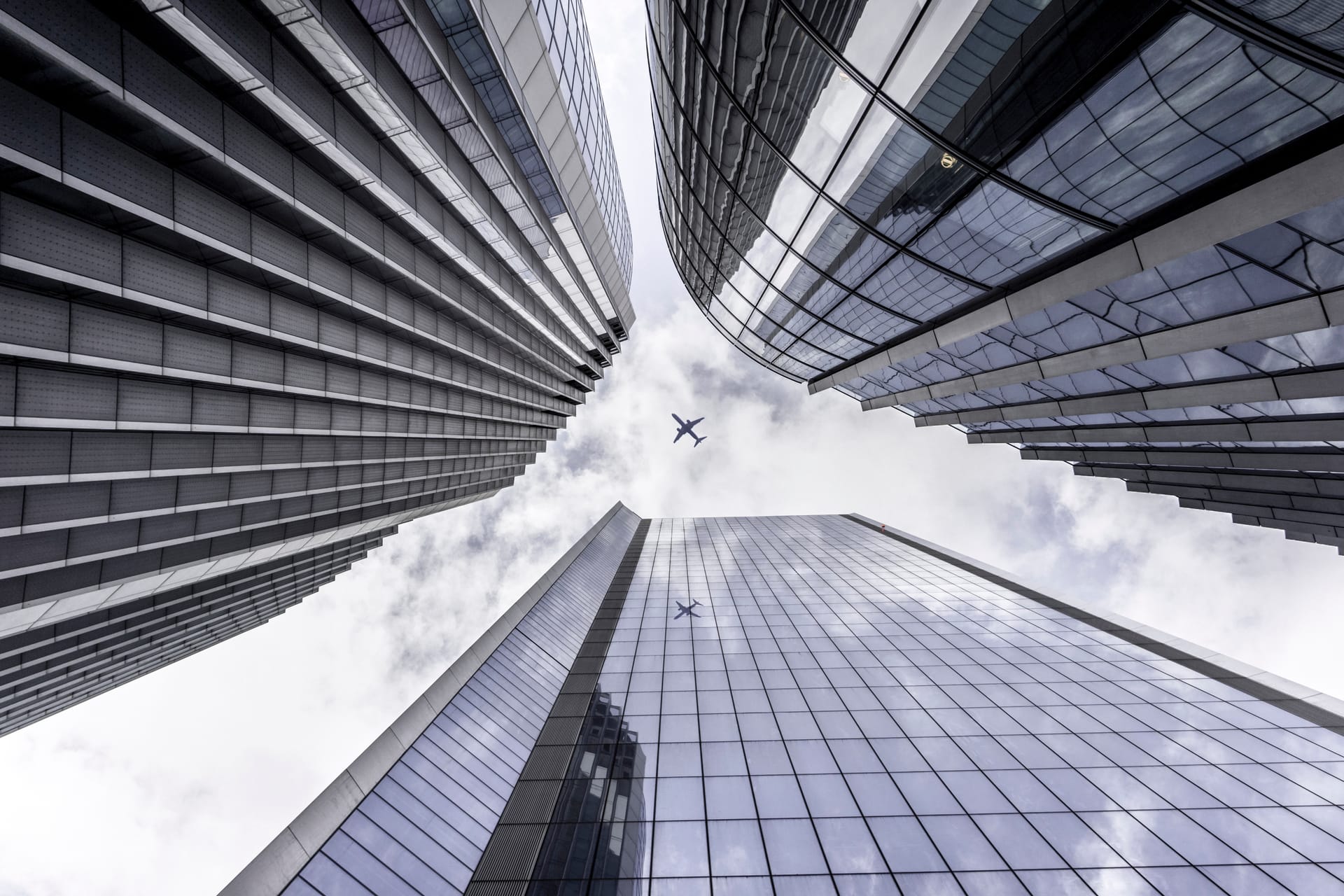 Three sky scrapers shown from below with plane flying overhead