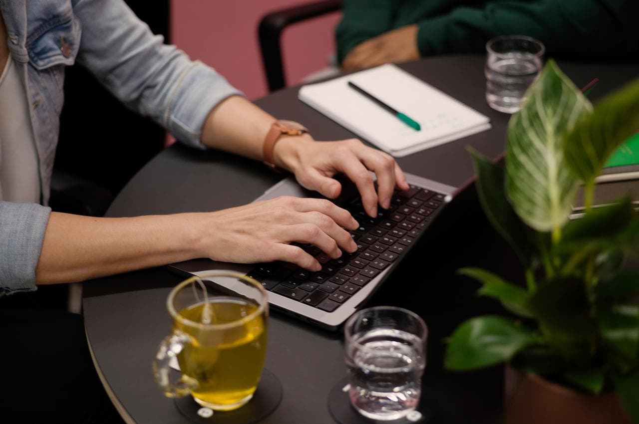 Close-up of a person's typing away on a keyboard at a desk.