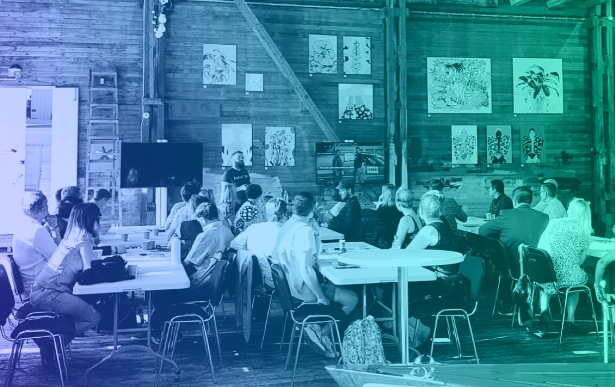 People attending a workshop in a wooden barn with artwork displayed on walls, bathed in blue-green lighting.