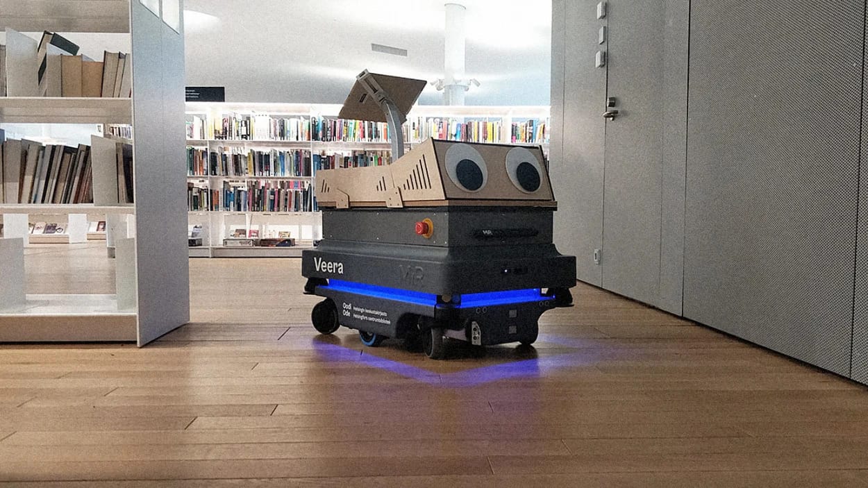 Robot named Veera with googly eyes and blue lighting navigating through a library with bookshelves in background.