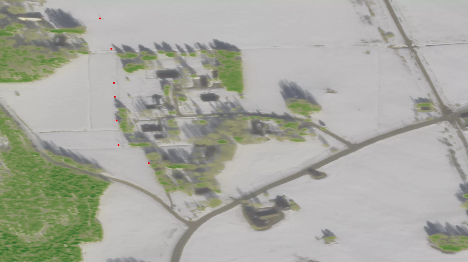 Aerial view of flooded rural area with buildings surrounded by water, green patches of land, and connecting roads.