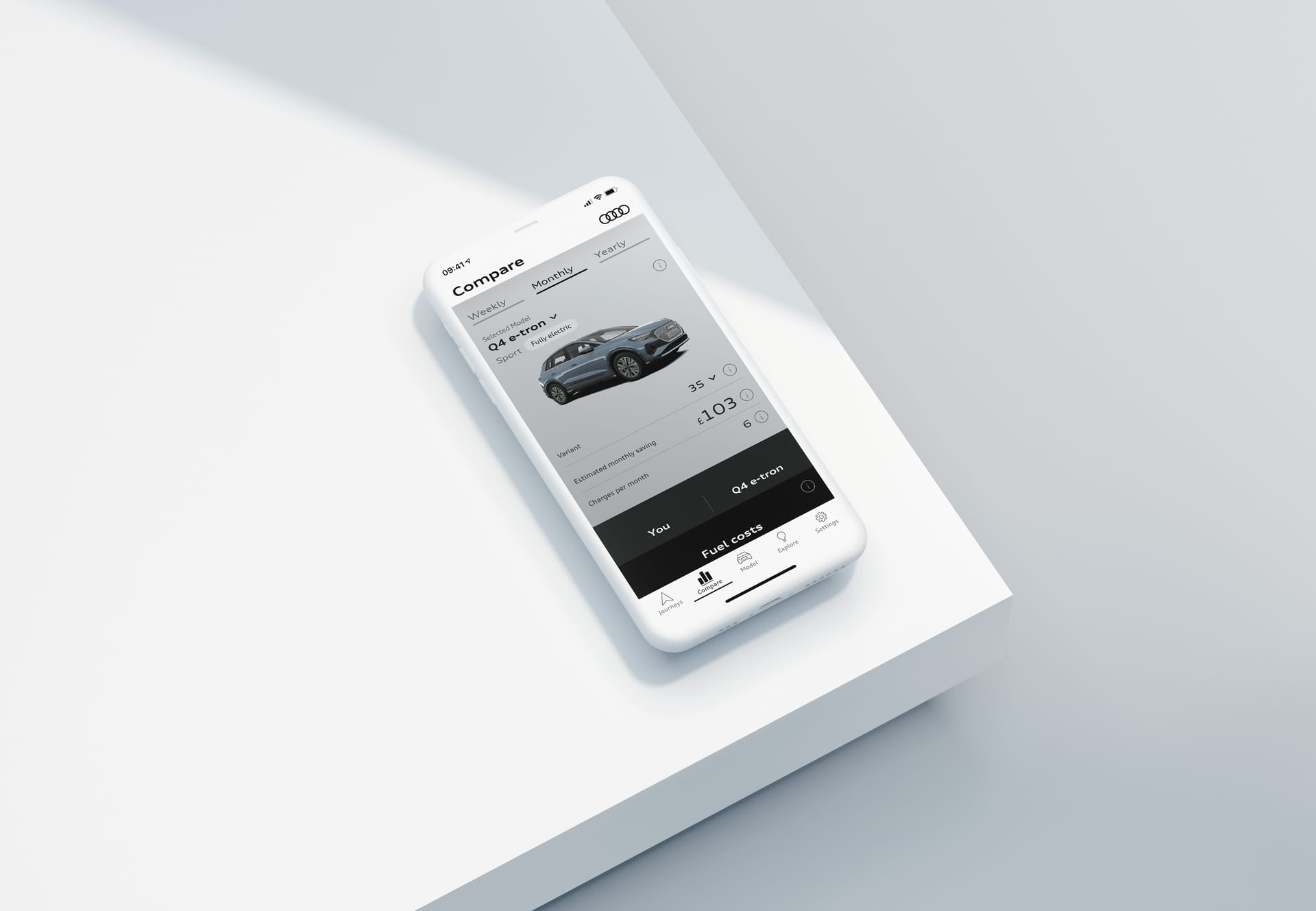 Smartphone displaying Audi app comparing Q4 e-tron vehicle costs and fuel expenses on a white surface.