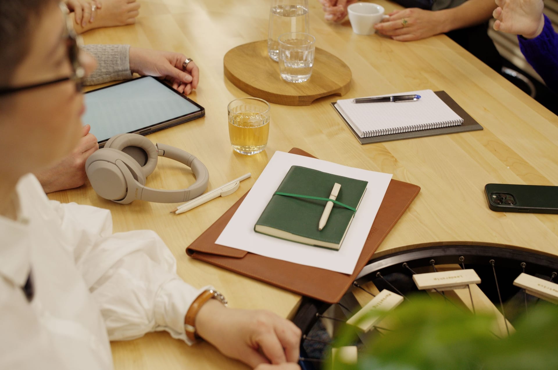 People gathered around wooden table with tablet, notebook, headphones, drinks and stationery during a meeting.