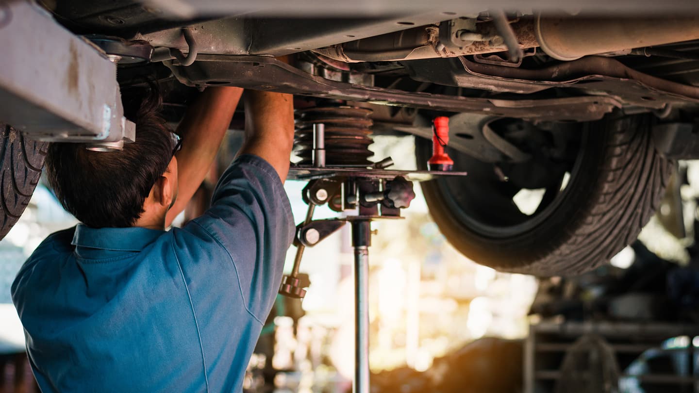 Colorized photo of a mechanic working on the underside of a car