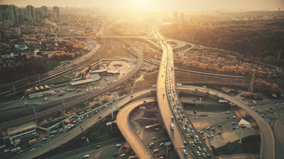 Aerial view of a city motorway interchange at sunset, with winding roads, traffic and high-rise buildings in golden light.