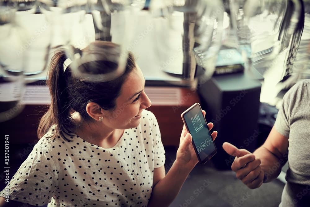 Woman in polka dot top looking at smartphone screen while conversing in a café setting.